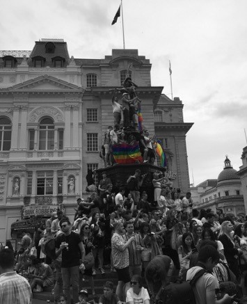 Back and white photo of London pride with coloured pride flags with people standing on monument